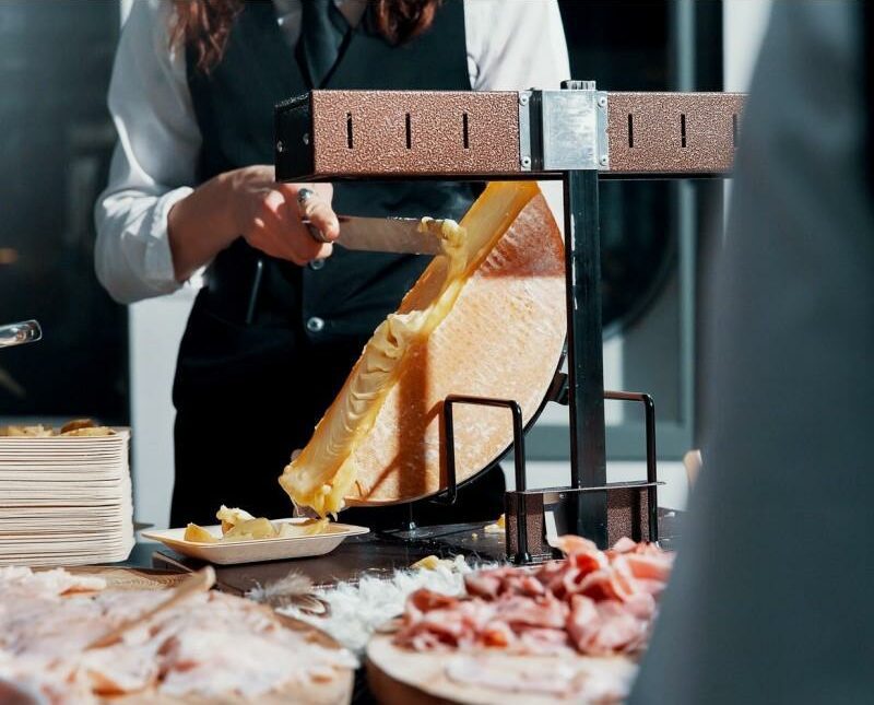 main d'un traiteur qui racle de la raclette dans une entreprise à paris.